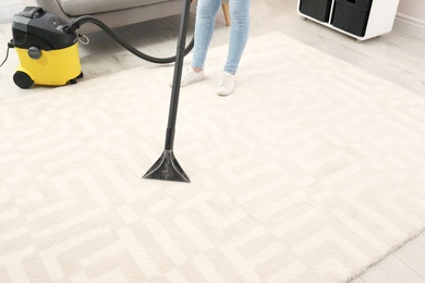 Woman removing dirt from carpet with vacuum cleaner indoors, closeup. Space for text