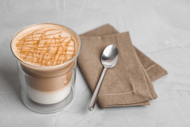 Photo of Glass with caramel macchiato, spoon and napkin on grey table