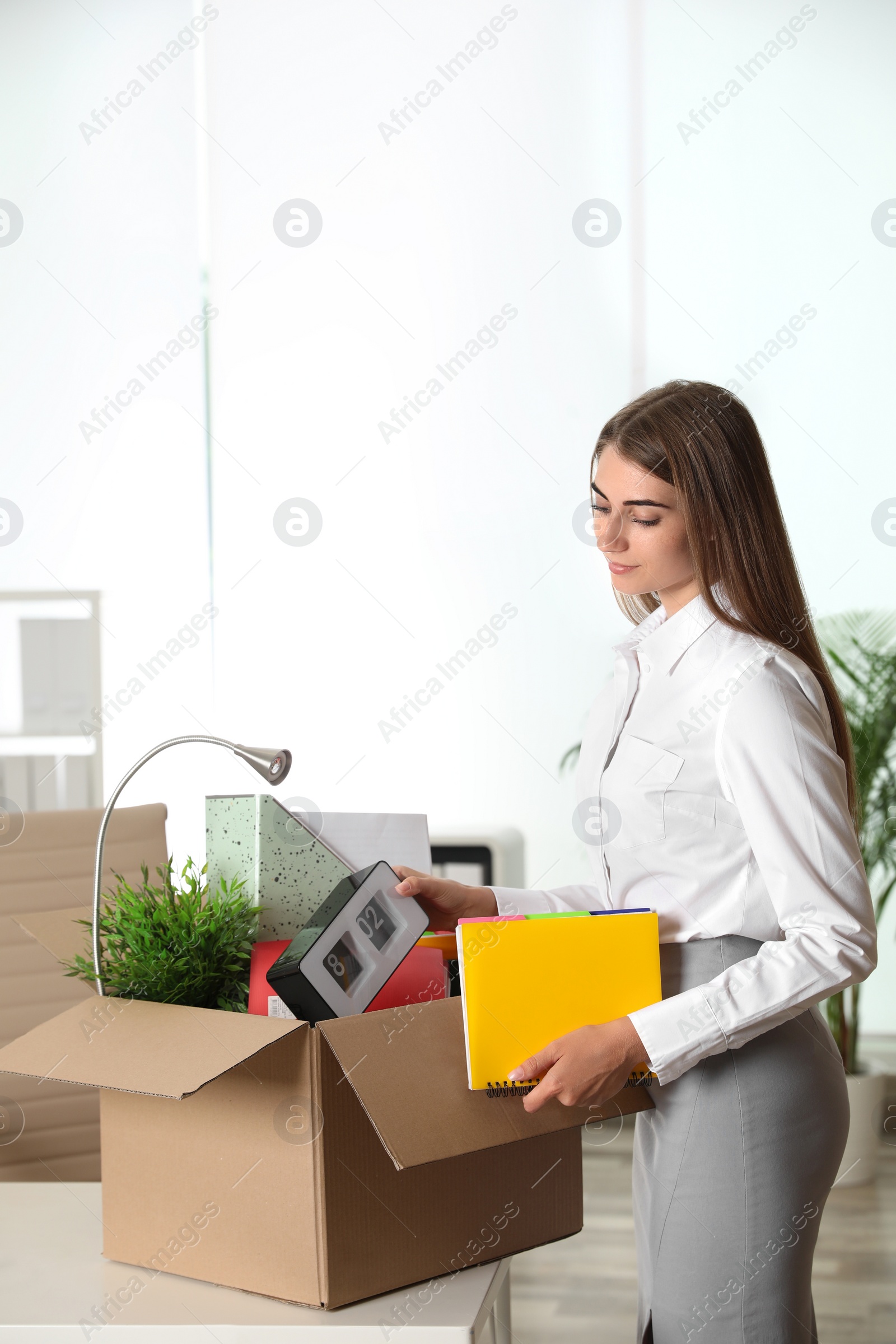 Photo of Happy young woman packing stuff in box at office