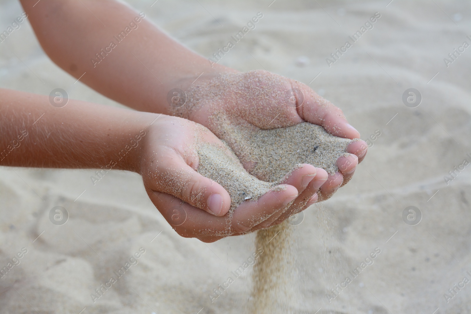 Photo of Child pouring sand from hands on beach, closeup. Fleeting time concept