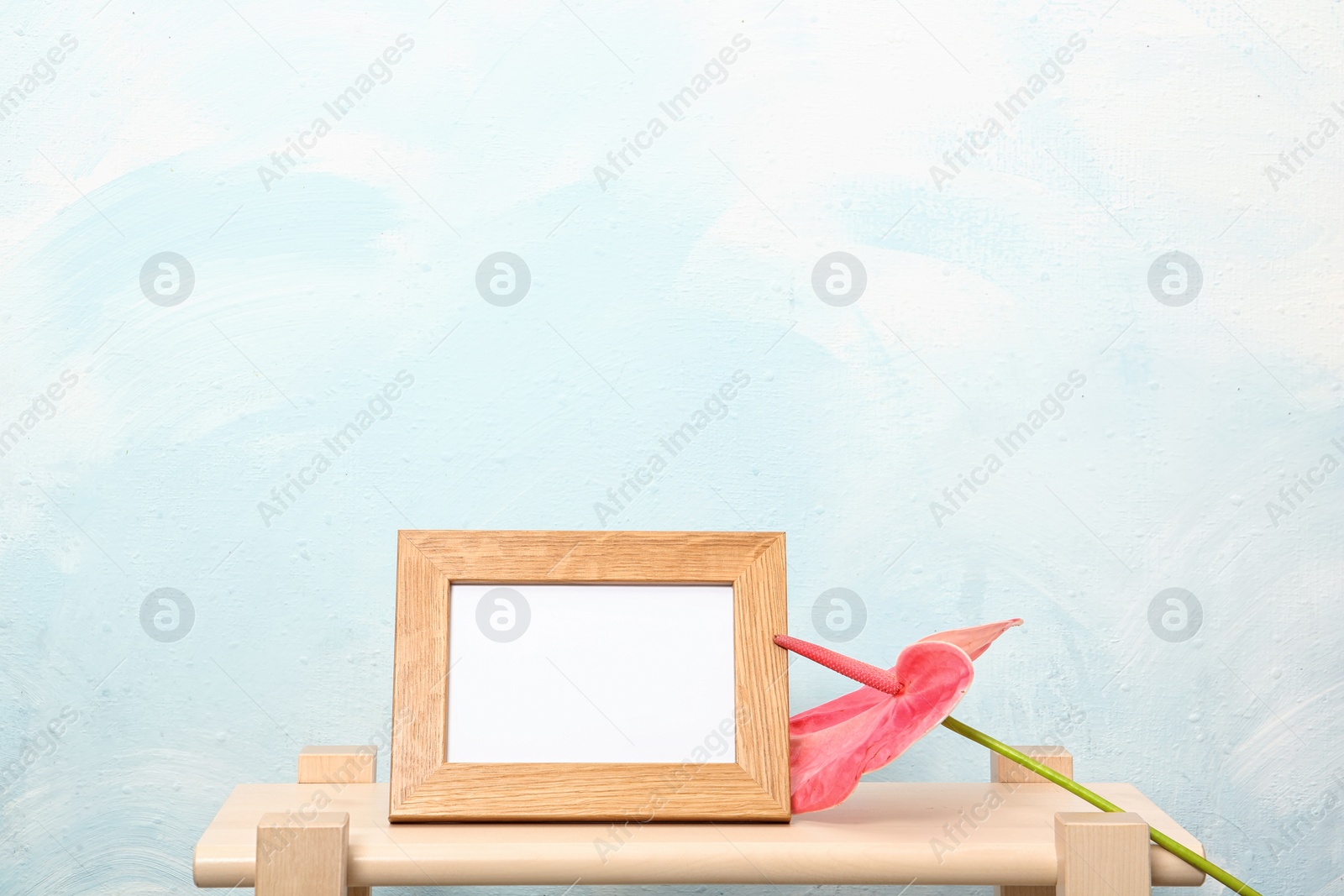 Photo of Blank frame and flower on table near light wall. Mock up for design