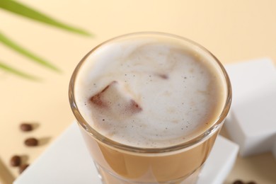 Photo of Refreshing iced coffee with milk in glass on pale yellow table, closeup