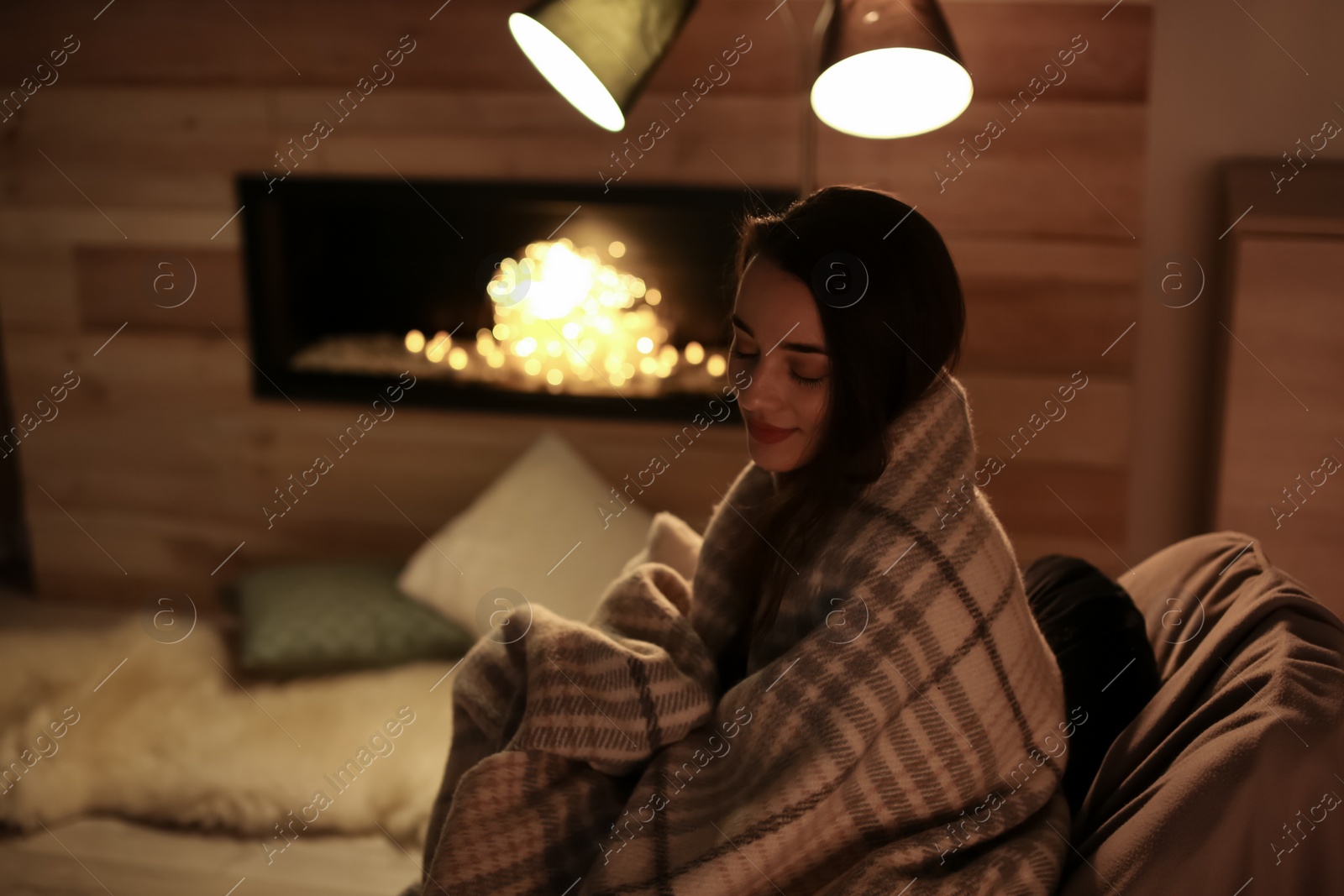 Photo of Young woman resting near decorative fireplace at home. Winter season