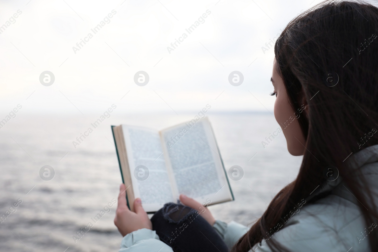 Photo of Woman reading book near river on cloudy day