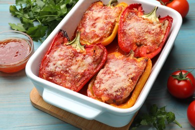 Photo of Tasty stuffed peppers in dish and ingredients on light blue wooden table, closeup