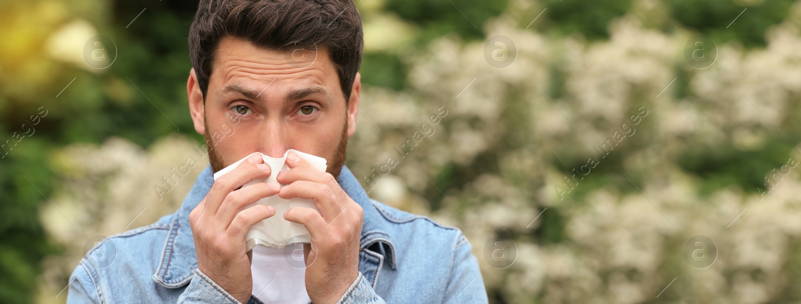 Image of Man suffering from seasonal spring allergy outdoors. Banner design with space for text