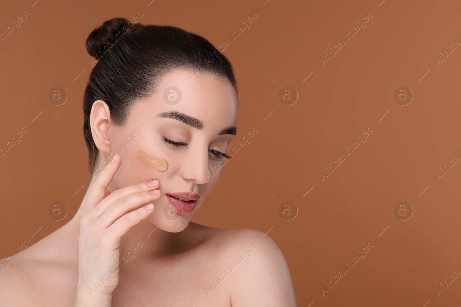 Photo of Woman with swatch of foundation on face against brown background. Space for text