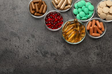 Photo of Different dietary supplements in glass bowls on grey table, flat lay. Space for text