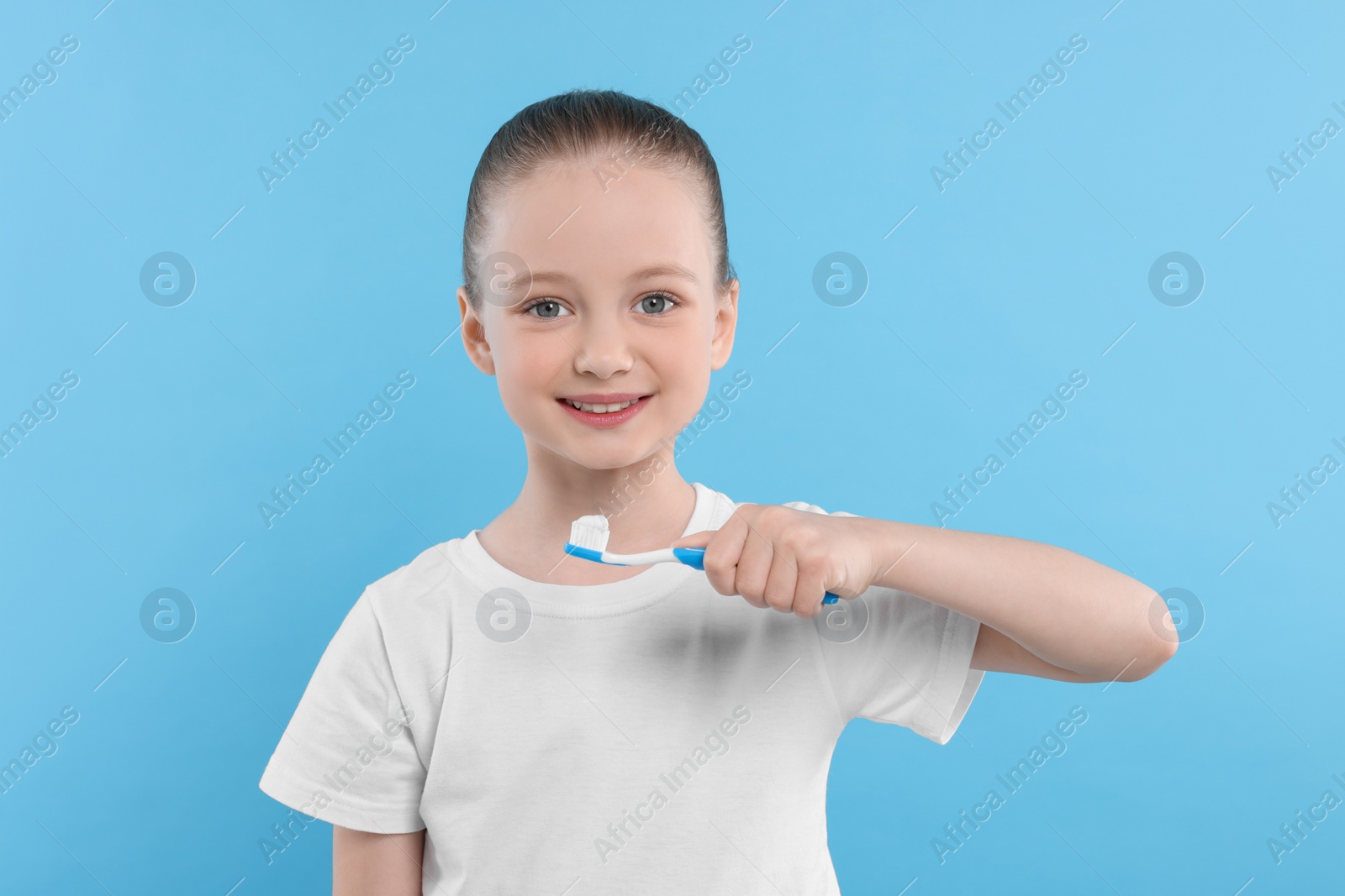 Photo of Happy girl brushing her teeth with toothbrush on light blue background