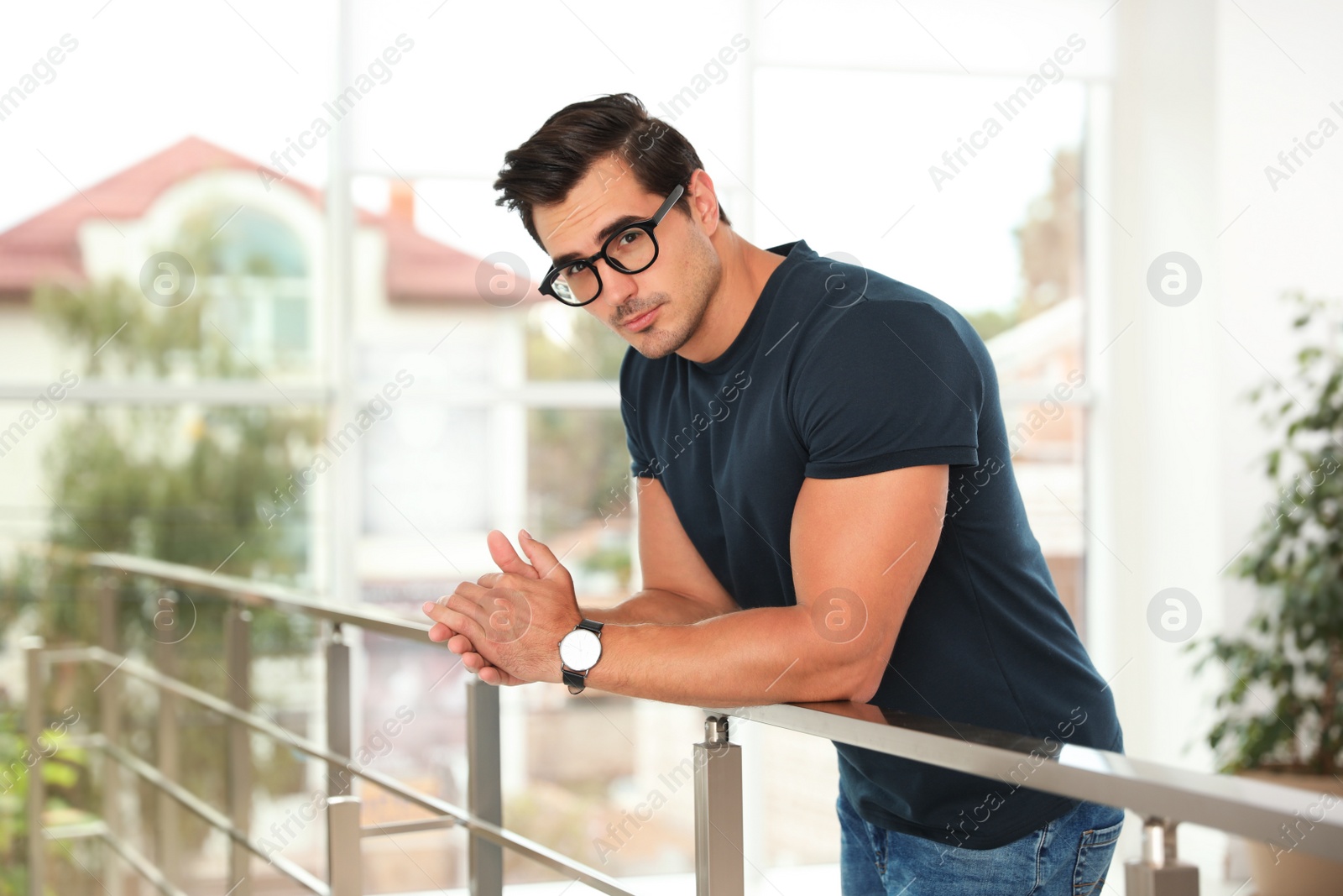 Photo of Portrait of handsome young man wearing glasses and leaning on railing indoors