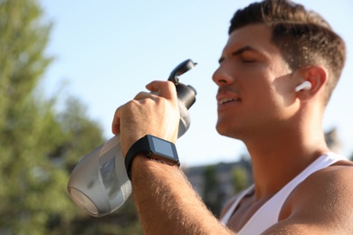 Photo of Man with fitness tracker drinking water after training outdoors, focus on hand