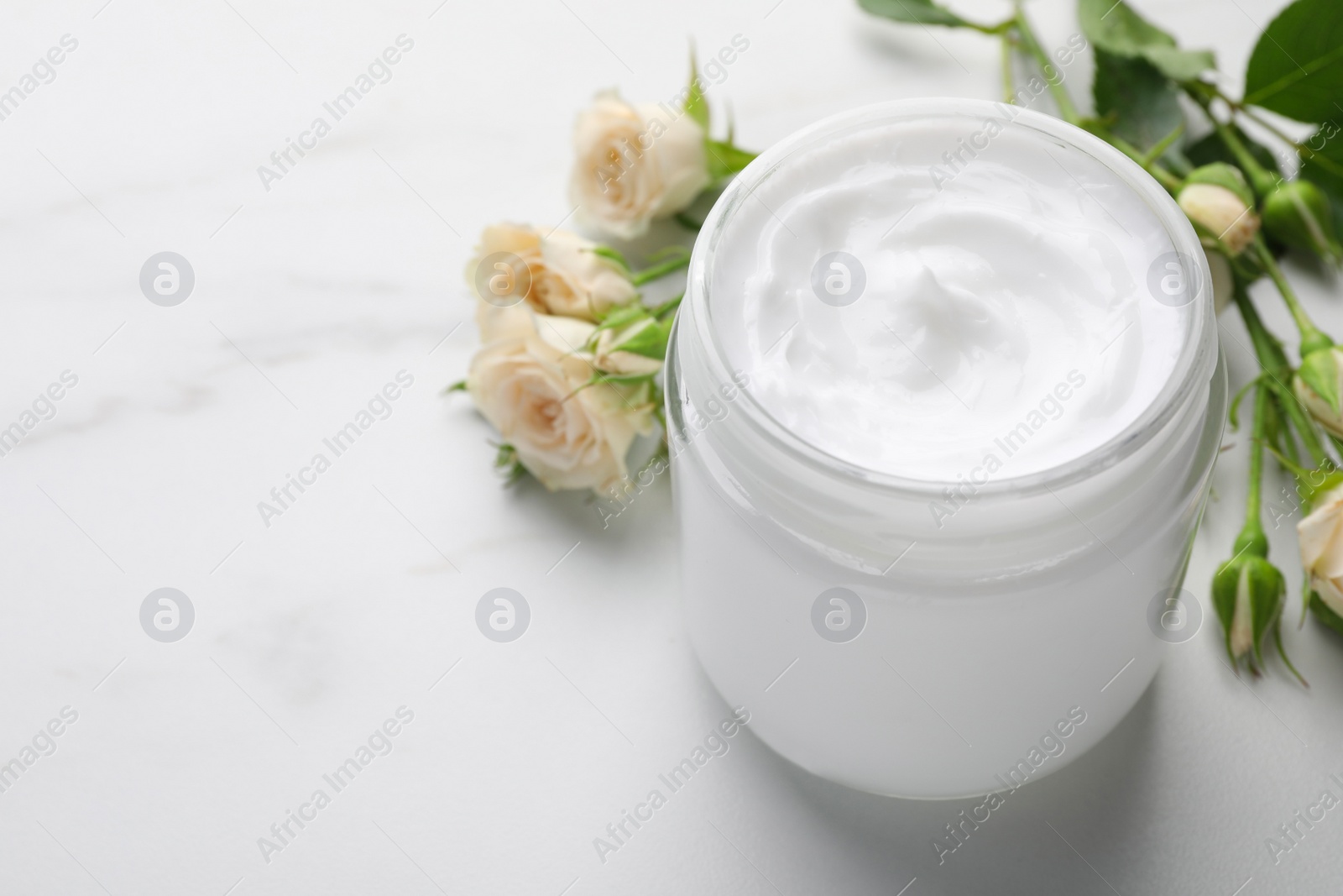 Photo of Jar of hand cream and roses on white marble table, space for text