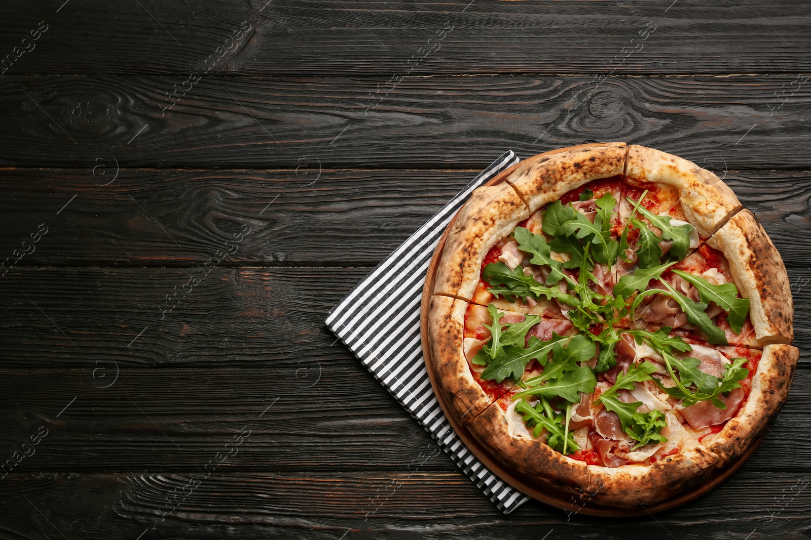 Photo of Tasty pizza with meat and arugula on black wooden table, top view. Space for text