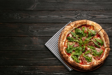 Photo of Tasty pizza with meat and arugula on black wooden table, top view. Space for text