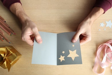 Man holding greeting card at wooden table, top view