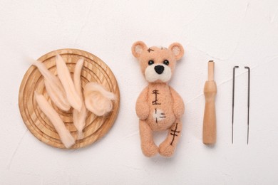 Photo of Felted bear, wool, needles and holder on white table, flat lay