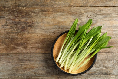 Photo of Plate with wild garlic or ramson on wooden table, top view. Space for text