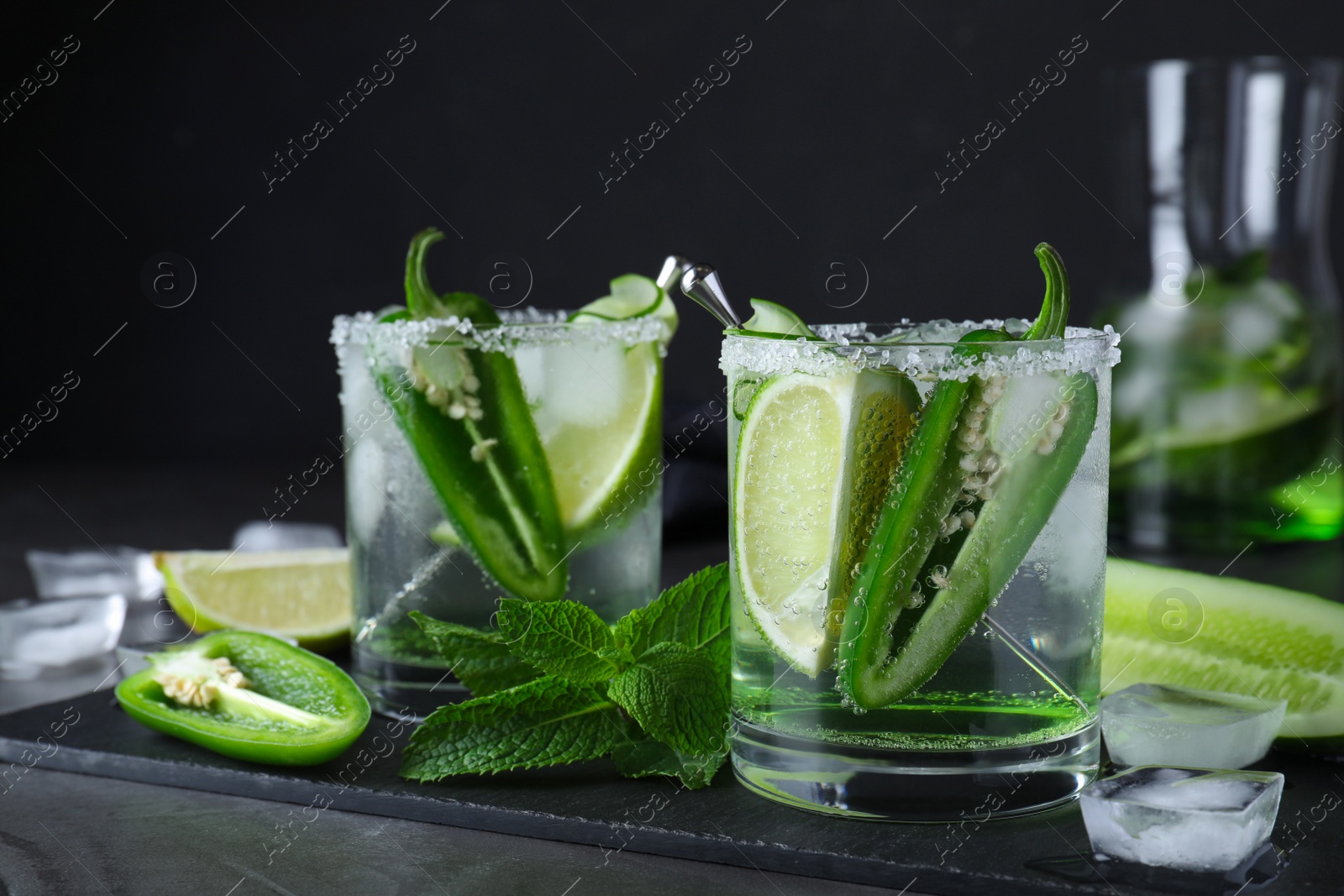 Photo of Spicy cocktail with jalapeno, cucumber and lime on black table