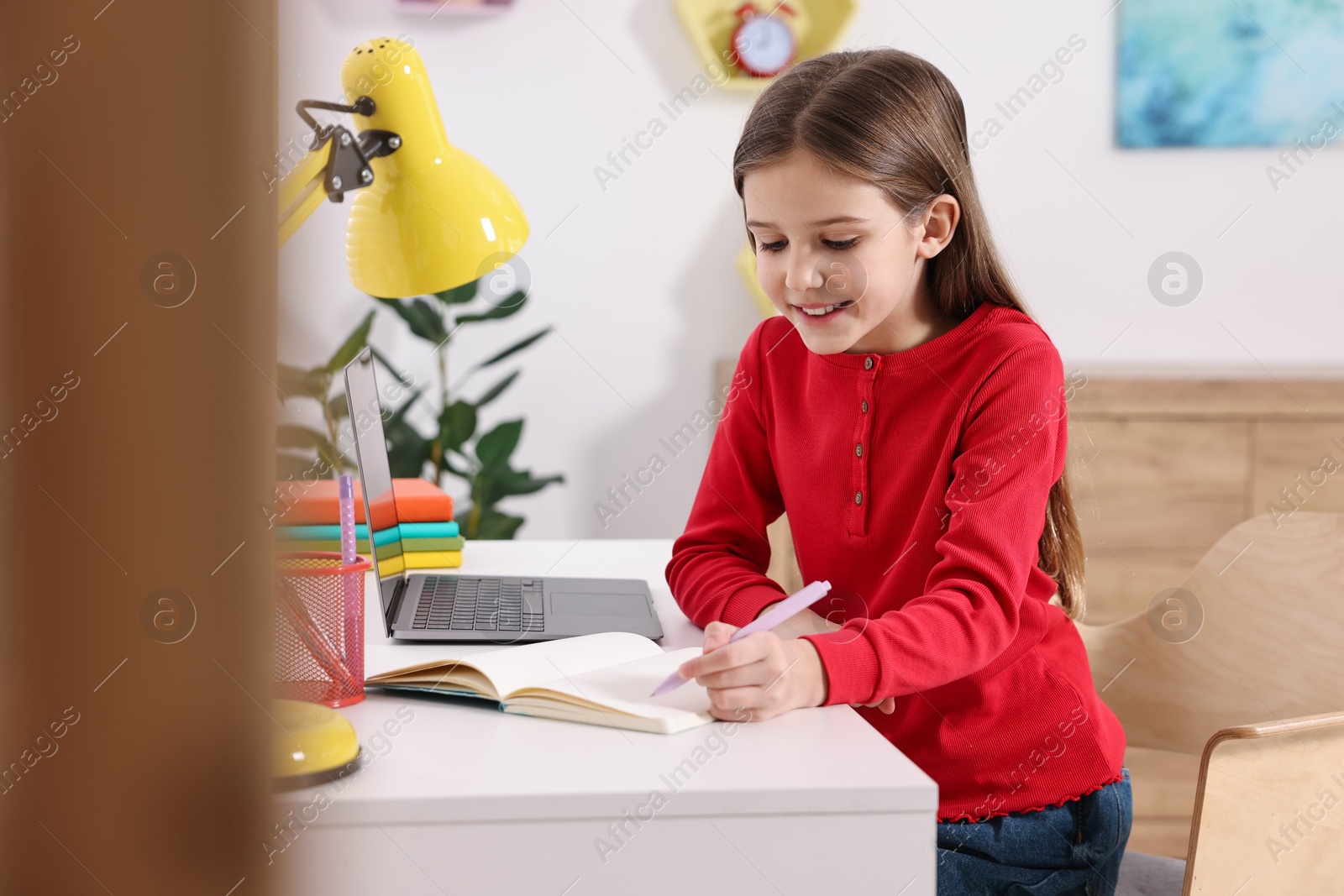 Photo of E-learning. Cute girl taking notes during online lesson at table indoors