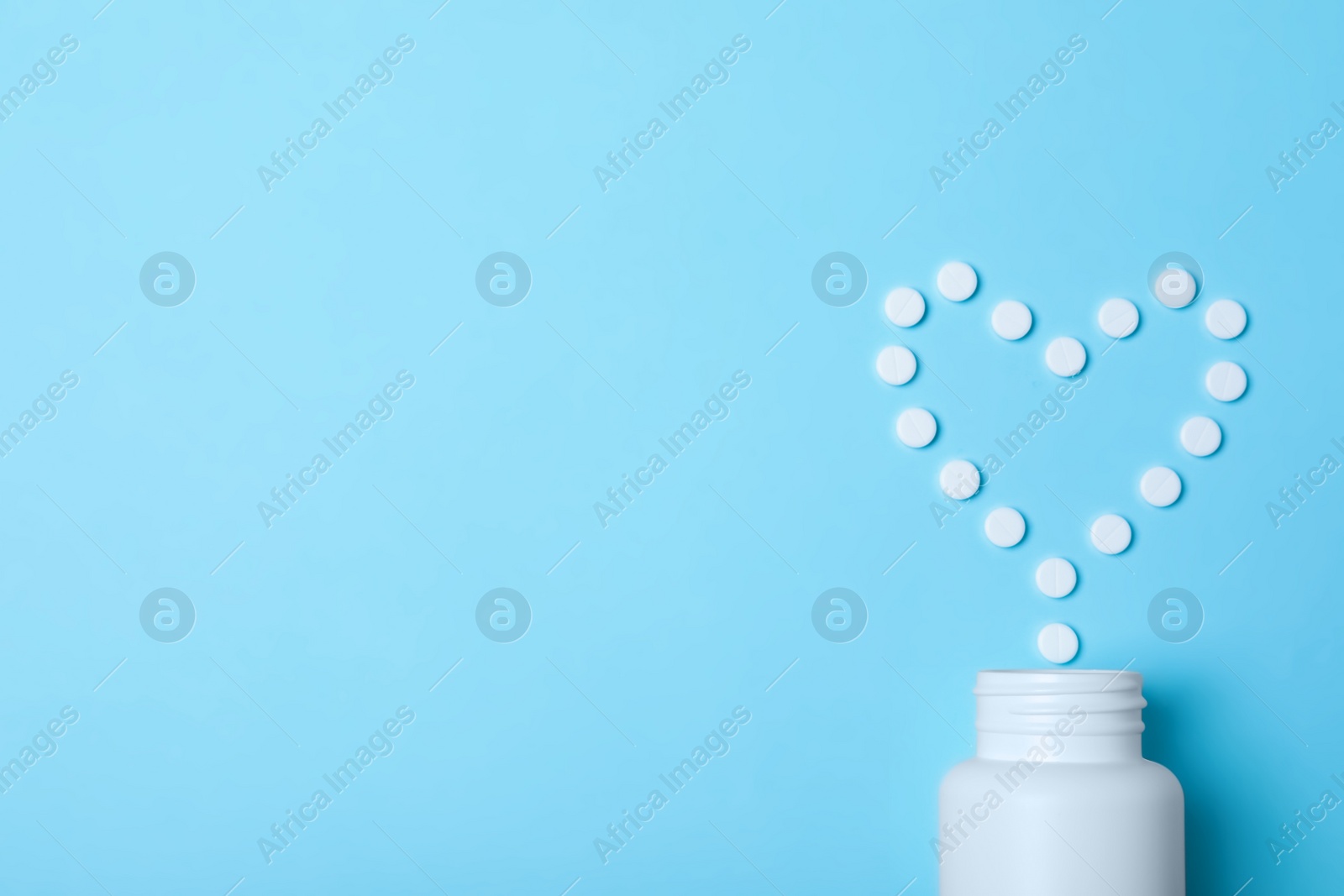 Photo of Heart made of pills and container on color background, top view with space for text. Cardiology concept