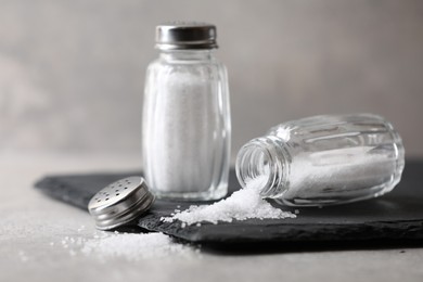 Photo of Natural salt in shakers on grey table, closeup