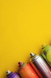 Photo of Used cans of spray paints on yellow background, flat lay with space for text. Graffiti supplies