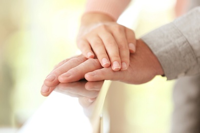 Photo of Young woman holding elderly man hand on railing indoors, closeup. Help service
