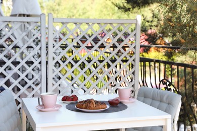 Photo of Outdoor breakfast with tea and croissants on white table on terrace