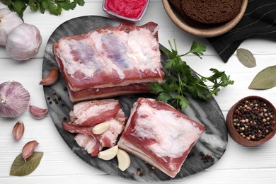 Photo of Pieces of tasty pork fatback with garlic and peppercorns on white wooden table, flat lay
