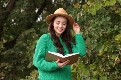 Photo of Beautiful young woman in stylish warm sweater reading book outdoors