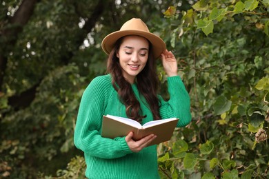 Beautiful young woman in stylish warm sweater reading book outdoors