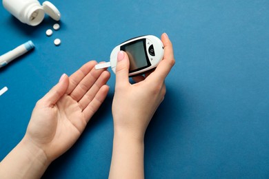 Diabetes. Woman checking blood sugar level with glucometer on blue background, top view. Space for text