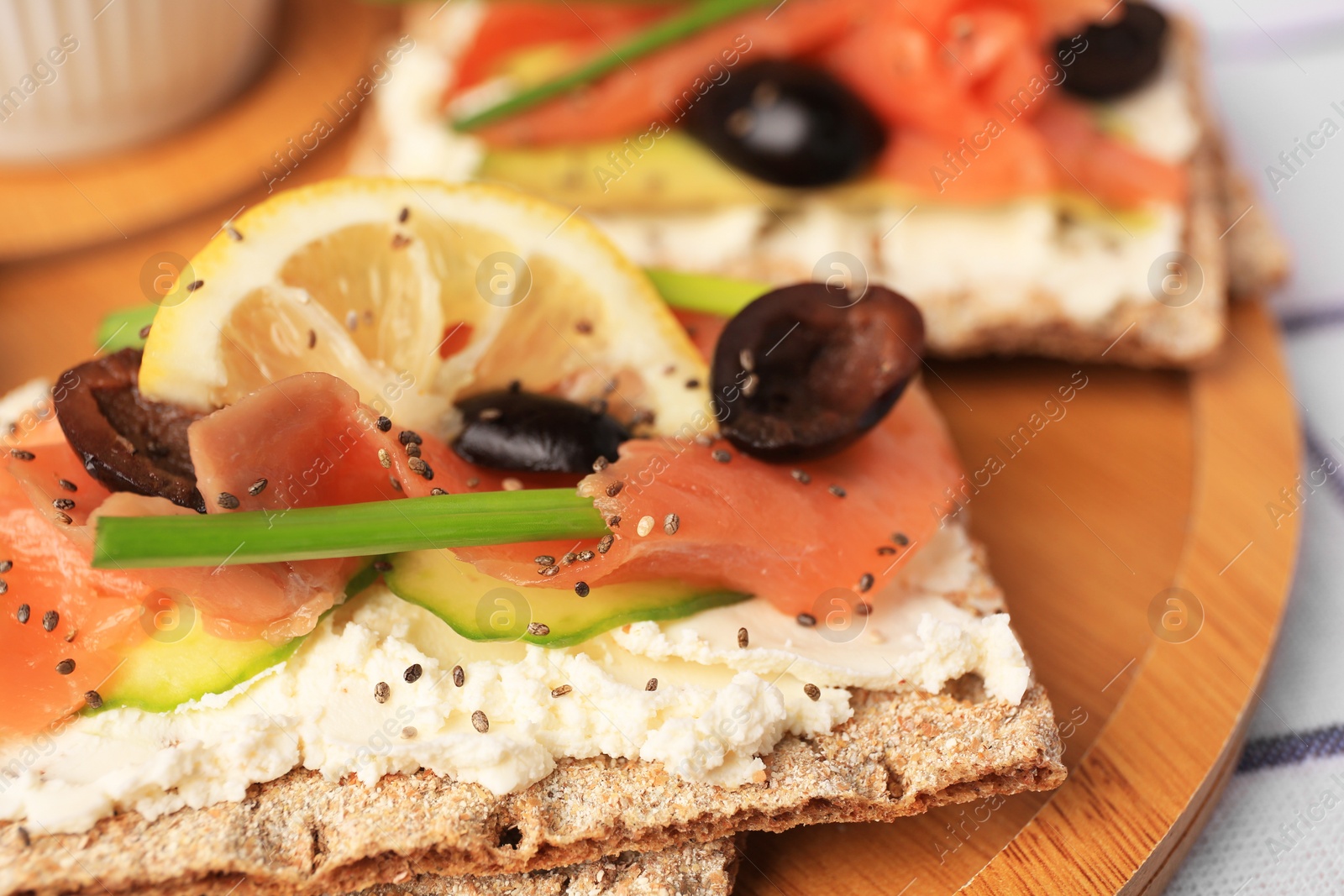 Photo of Fresh crunchy crispbreads with cream cheese, salmon, olives, lemon and green onion on wooden board, closeup