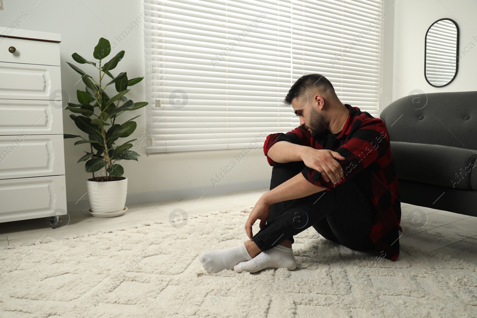 Photo of Sad man sitting on floor at home. Space for text