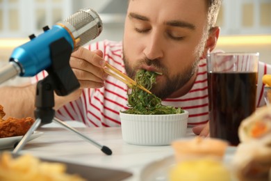 Photo of Food blogger eating near microphone at table in kitchen, closeup. Mukbang vlog