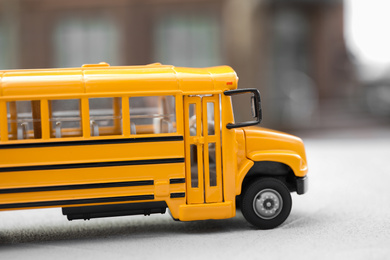 Photo of Yellow toy school bus against blurred 
background, closeup. Transport for students