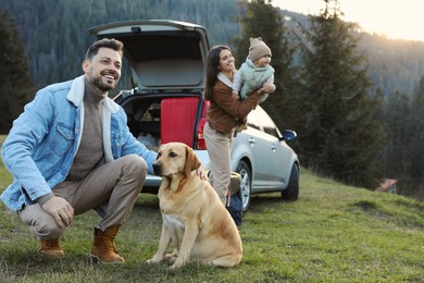 Photo of Happy man with dog, mother and her daughter near car in mountains. Family traveling with pet