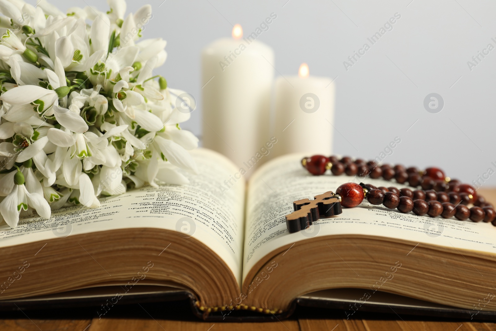Photo of Bible, rosary beads, flowers and church candles on wooden table, closeup
