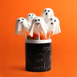Photo of Delicious ghost shaped cake pops on orange background. Halloween celebration