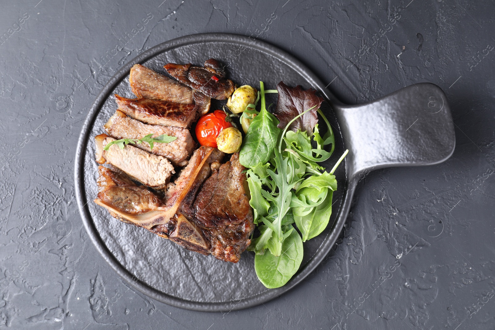 Photo of Delicious grilled beef meat, vegetables and greens on black table, top view