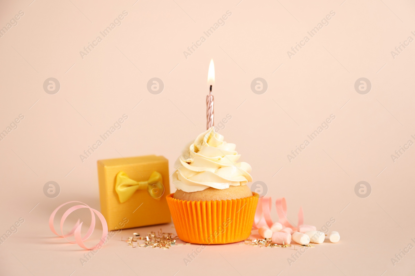 Photo of Delicious birthday cupcake with burning candle, marshmallows and gift box on beige background