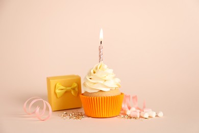 Delicious birthday cupcake with burning candle, marshmallows and gift box on beige background