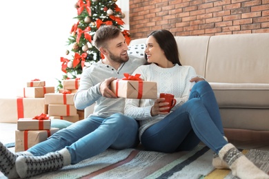 Photo of Young man giving Christmas gift to his girlfriend at home