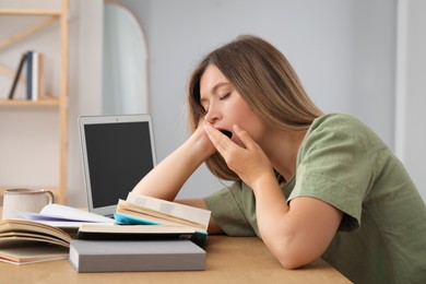 Photo of Sleepy young woman studying at wooden table indoors