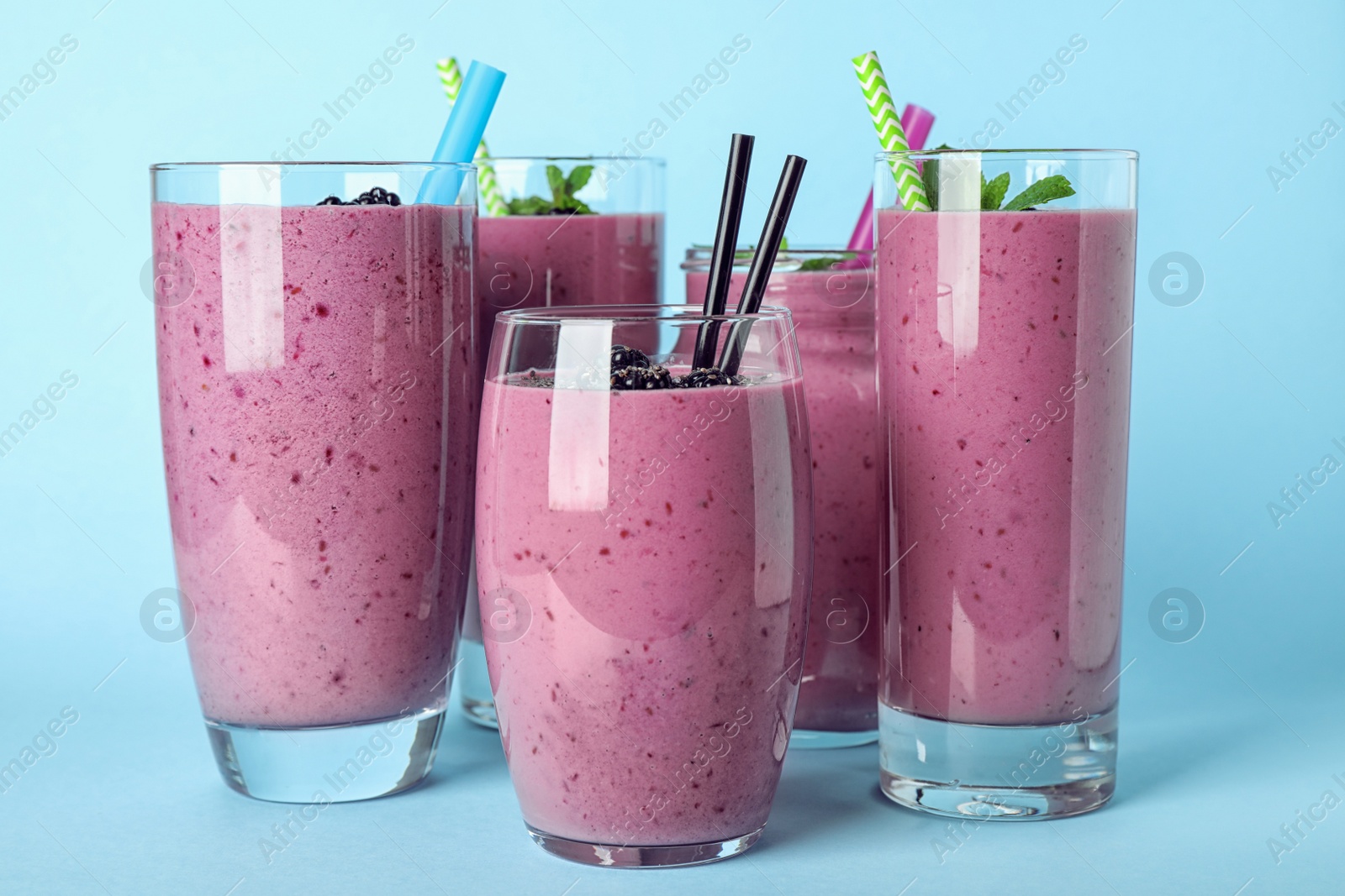 Photo of Delicious blackberry smoothie in different glassware on light blue background