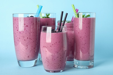 Photo of Delicious blackberry smoothie in different glassware on light blue background