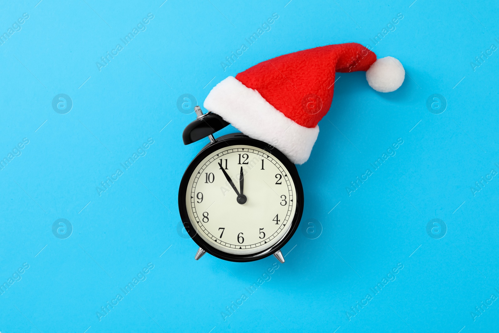 Photo of Alarm clock in Santa hat on light blue background, top view. New Year countdown