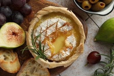 Tasty baked brie cheese and products on light tiled table, flat lay
