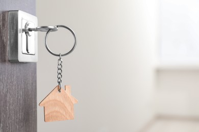 Photo of Mortgage and real estate. Open door with key and house shaped keychain against blurred background, space for text