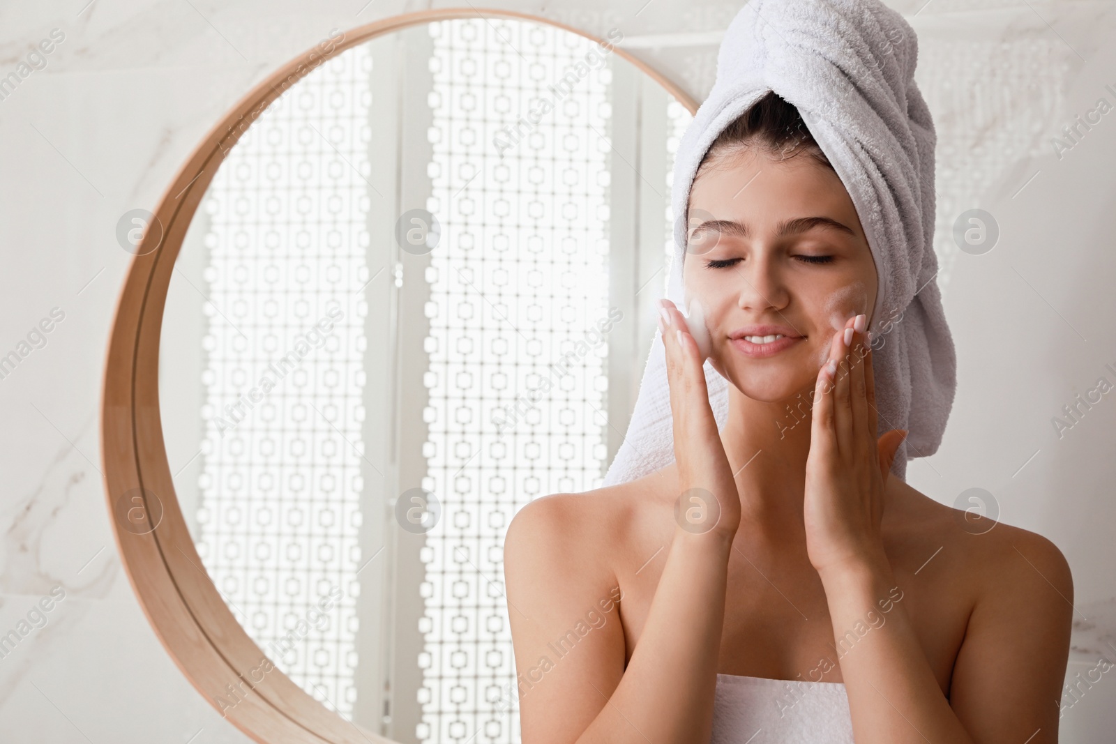 Photo of Beautiful teenage girl applying cleansing foam onto face in bathroom, space for text. Skin care cosmetic